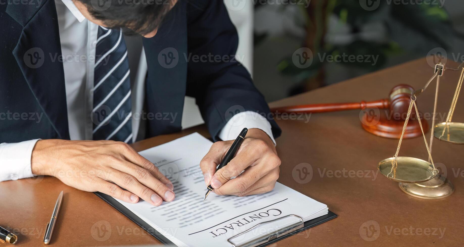 Lawyer reviewing and signing contract documents with gavel and scales of justice on desk. photo