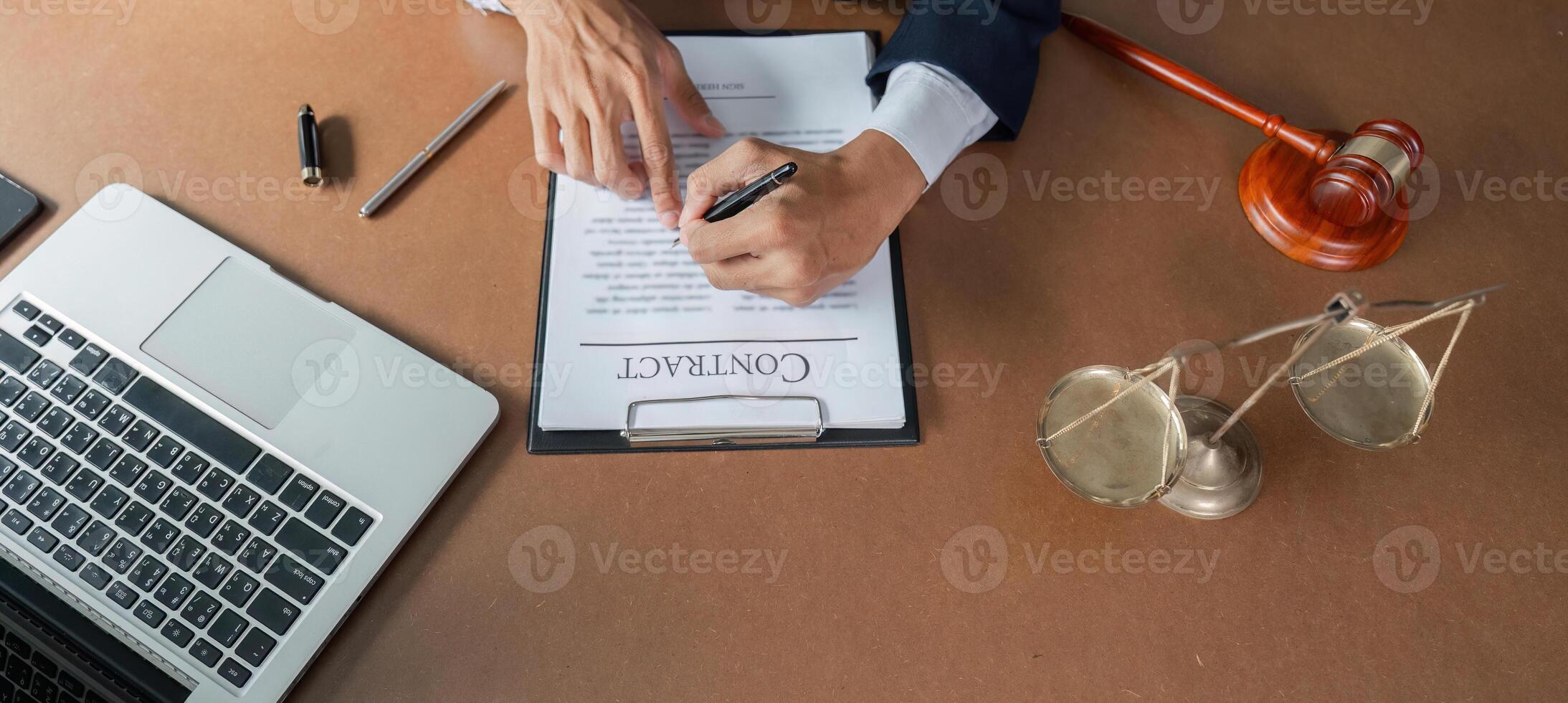 Lawyer signing contract document while reviewing legal paperwork at desk with laptop and gavel. photo