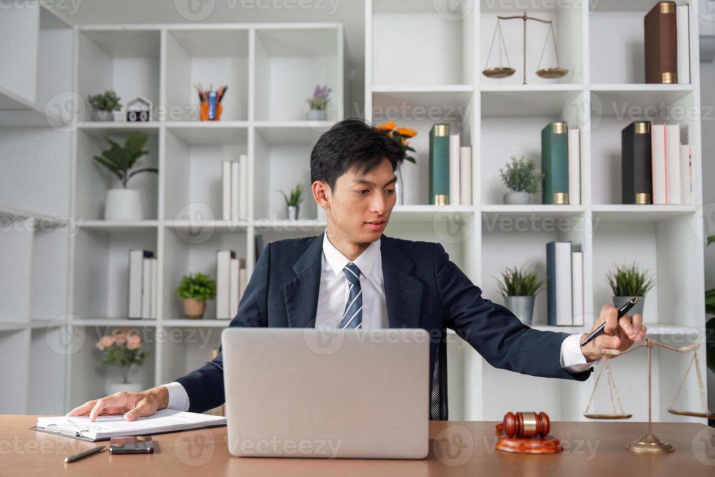 Asian lawyer analyzing case files while balancing scales of justice in modern office environment. photo