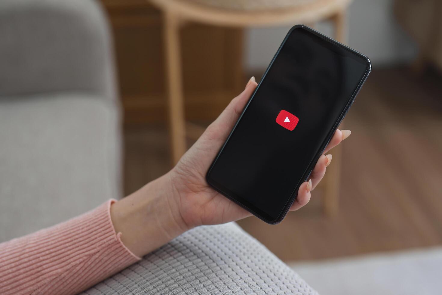 CHIANG MAI, THAILAND - FEB 27 2025. Person holding smartphone with YouTube logo on screen, relaxing at home. photo