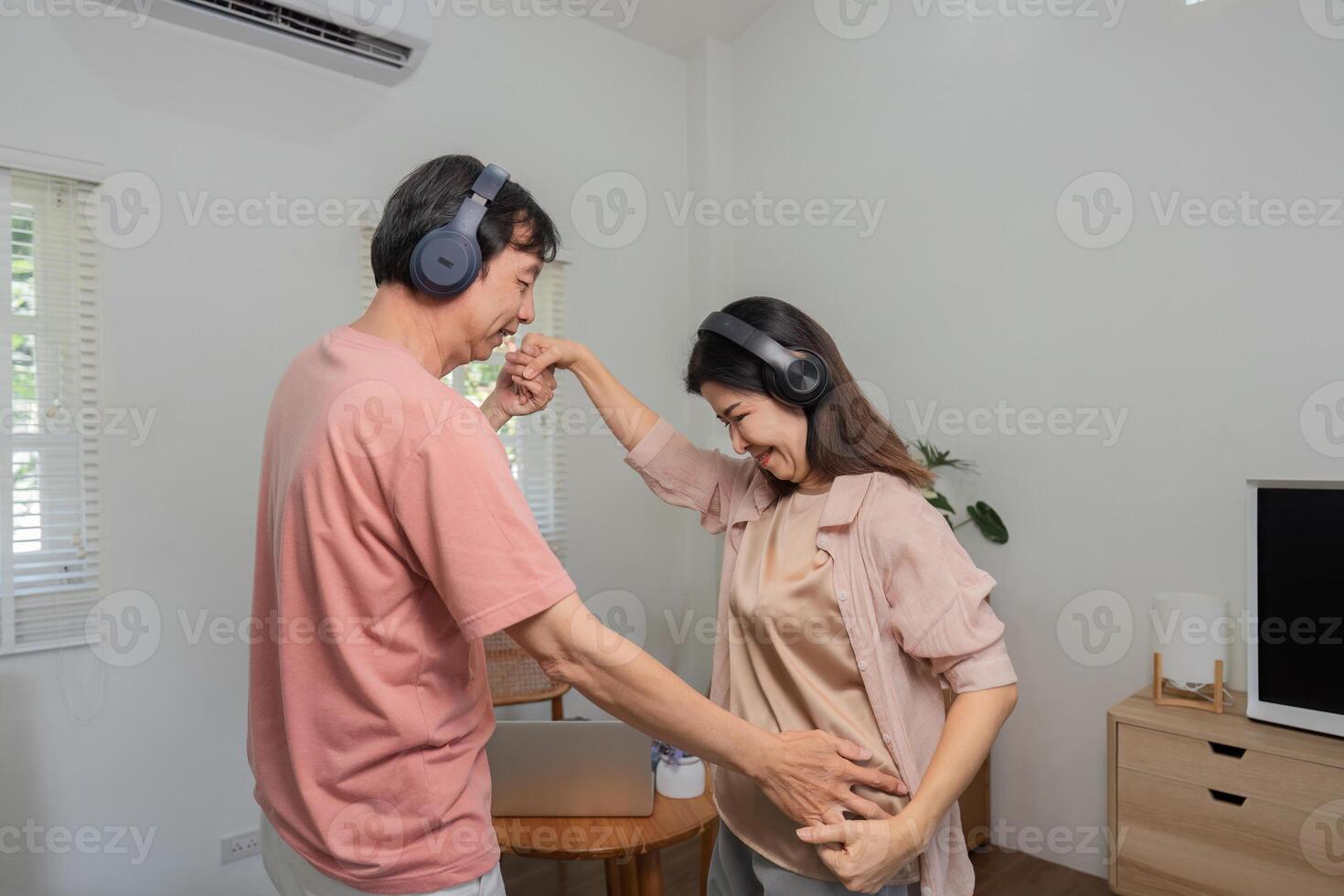 Senior couple enjoying a playful dance while listening to music with headphones at home. photo