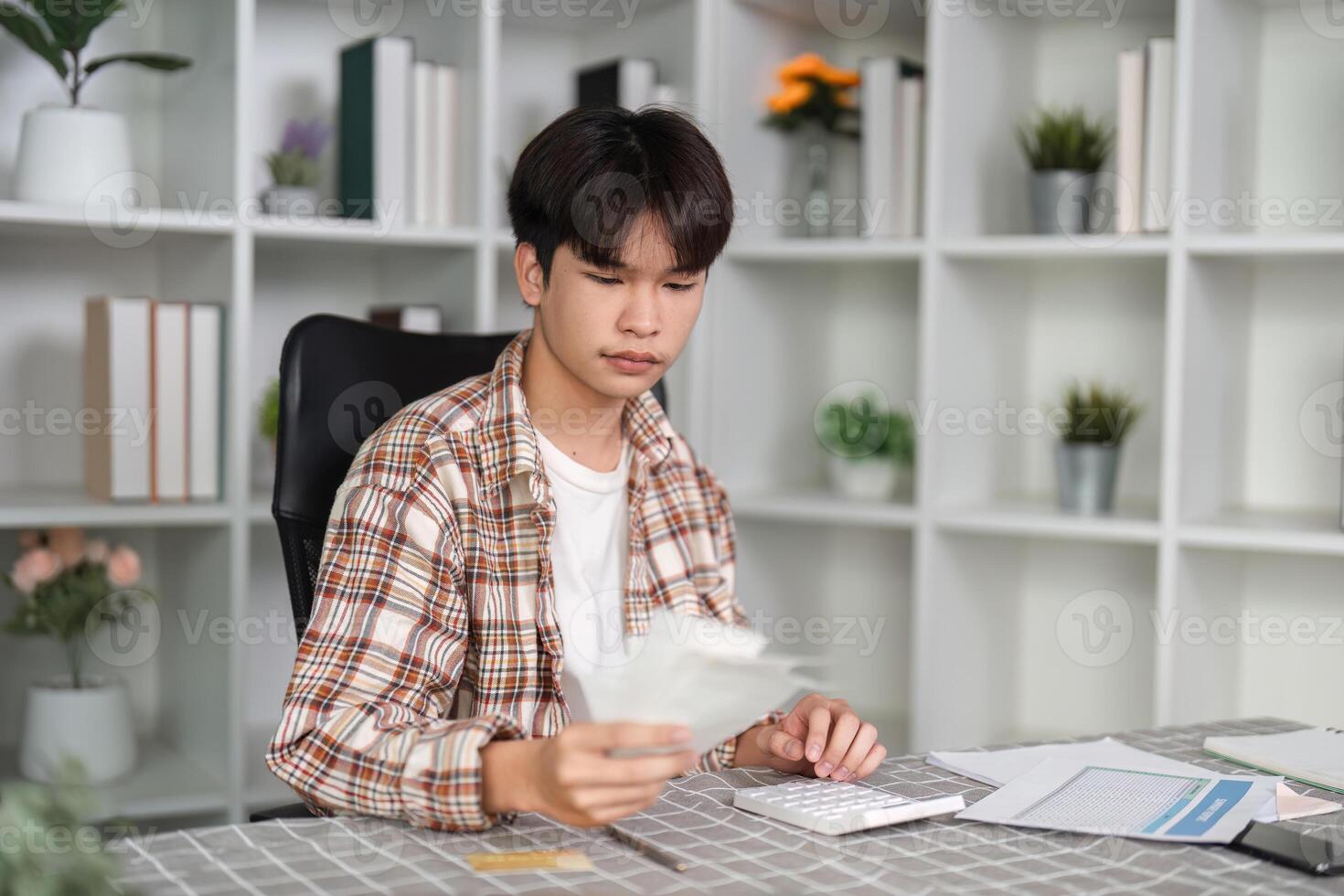 Young man managing finances at home, reviewing bills and using a calculator in a modern workspace. photo