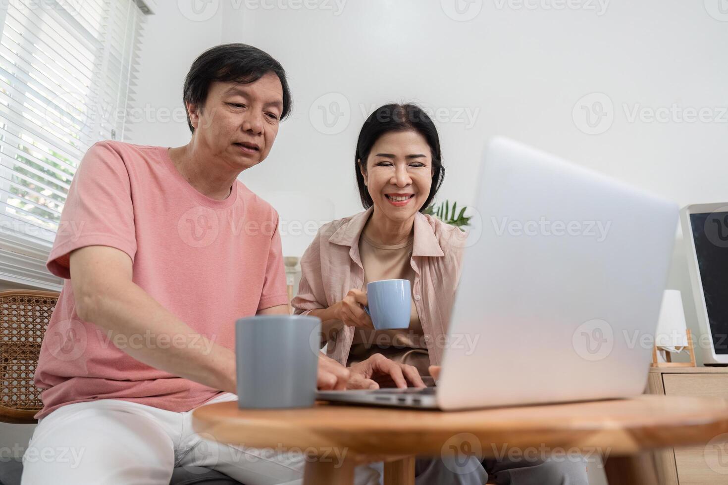 Senior couple enjoying coffee while exploring content on a laptop at home. photo