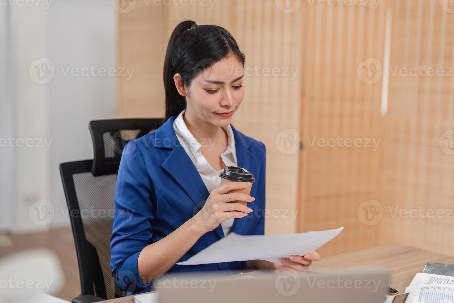 Professional businesswoman studying financial documents while sipping coffee, preparing for tax obligations. photo