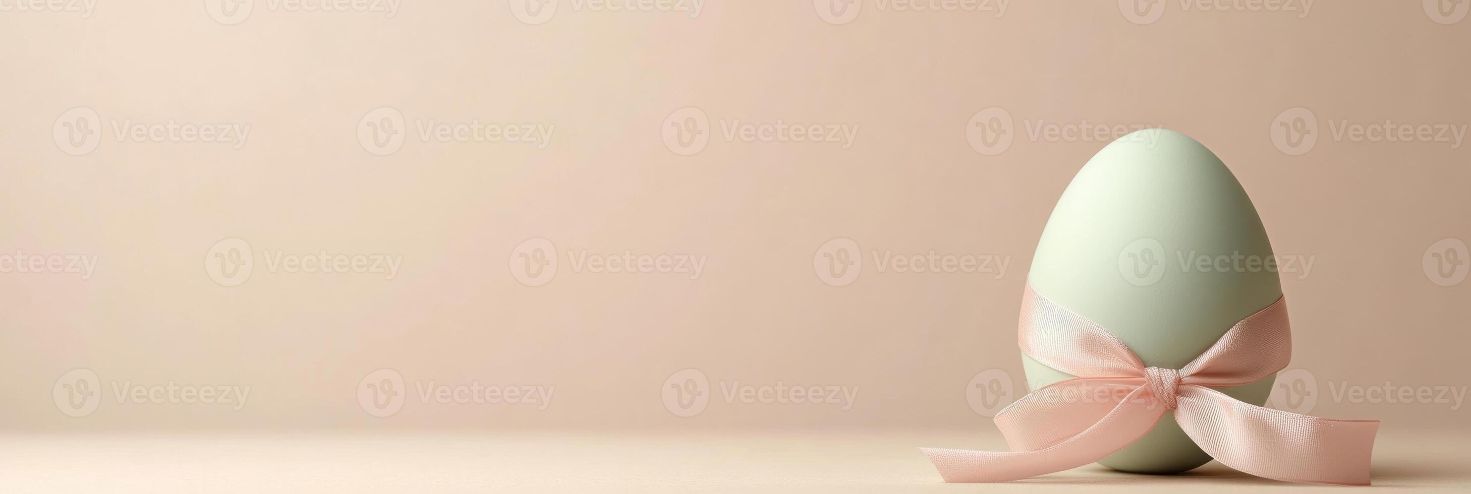 Green easter egg with pink ribbon bow on pastel background for holiday concept photo