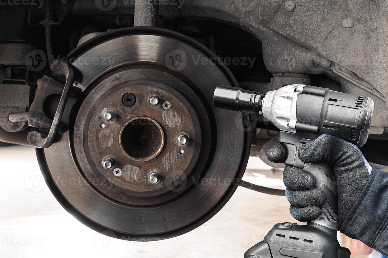 Close up of brake disc and impact wrench cordless , A mechanic is using a cordless impact wrench to repair a car rear brake system , Car repair concept photo