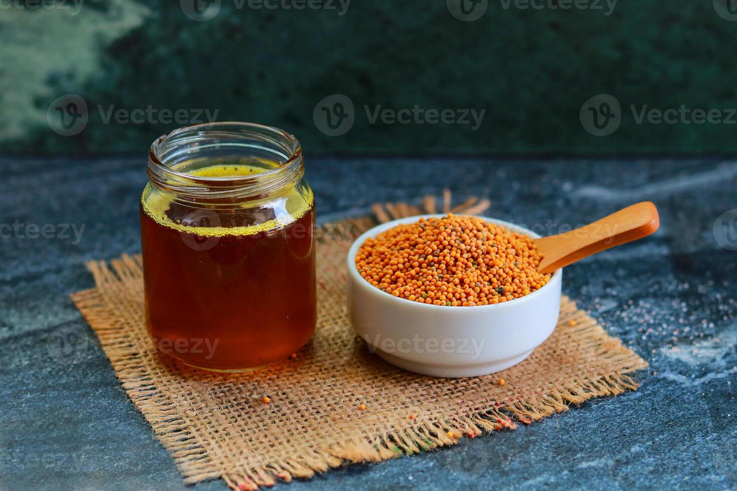 A white bowl of Mustard seeds and wooden spoon and a jar of Mustard oil on a table photo