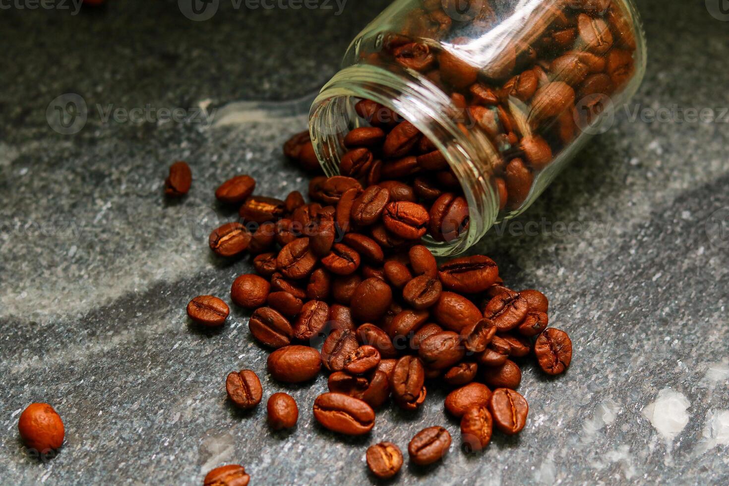 Coffee beans spilling out of a glass jar on a stone background photo
