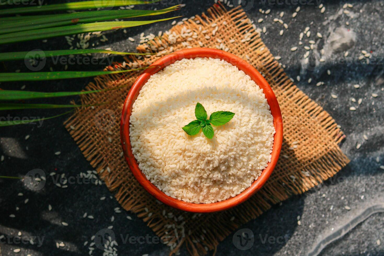 Bowl with uncooked rice and basil on the table, top view photo