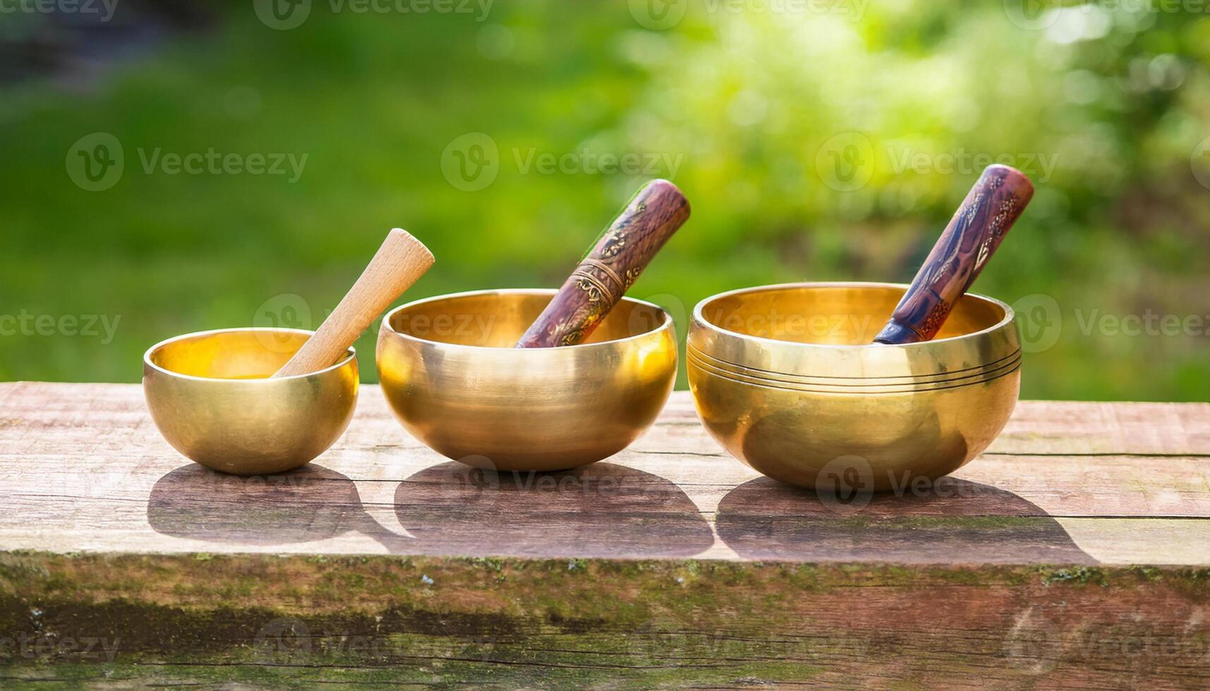 Singing bowl for sound healing session in green garden on wooden table. Alternative health medicine photo