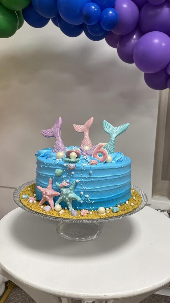 Mermaid themed birthday cake with chocolate mermaid tails, seashells, pearls, and a 6 candle. Party decorations photo