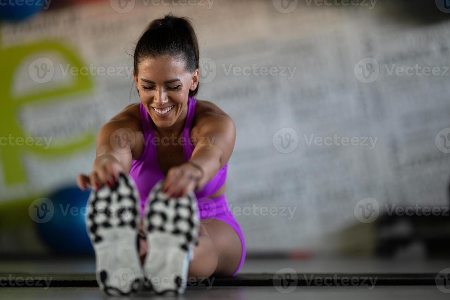 Woman Stretching in Gym. A athletic woman wearing a purple sports outfit is stretching her legs in a gym. photo