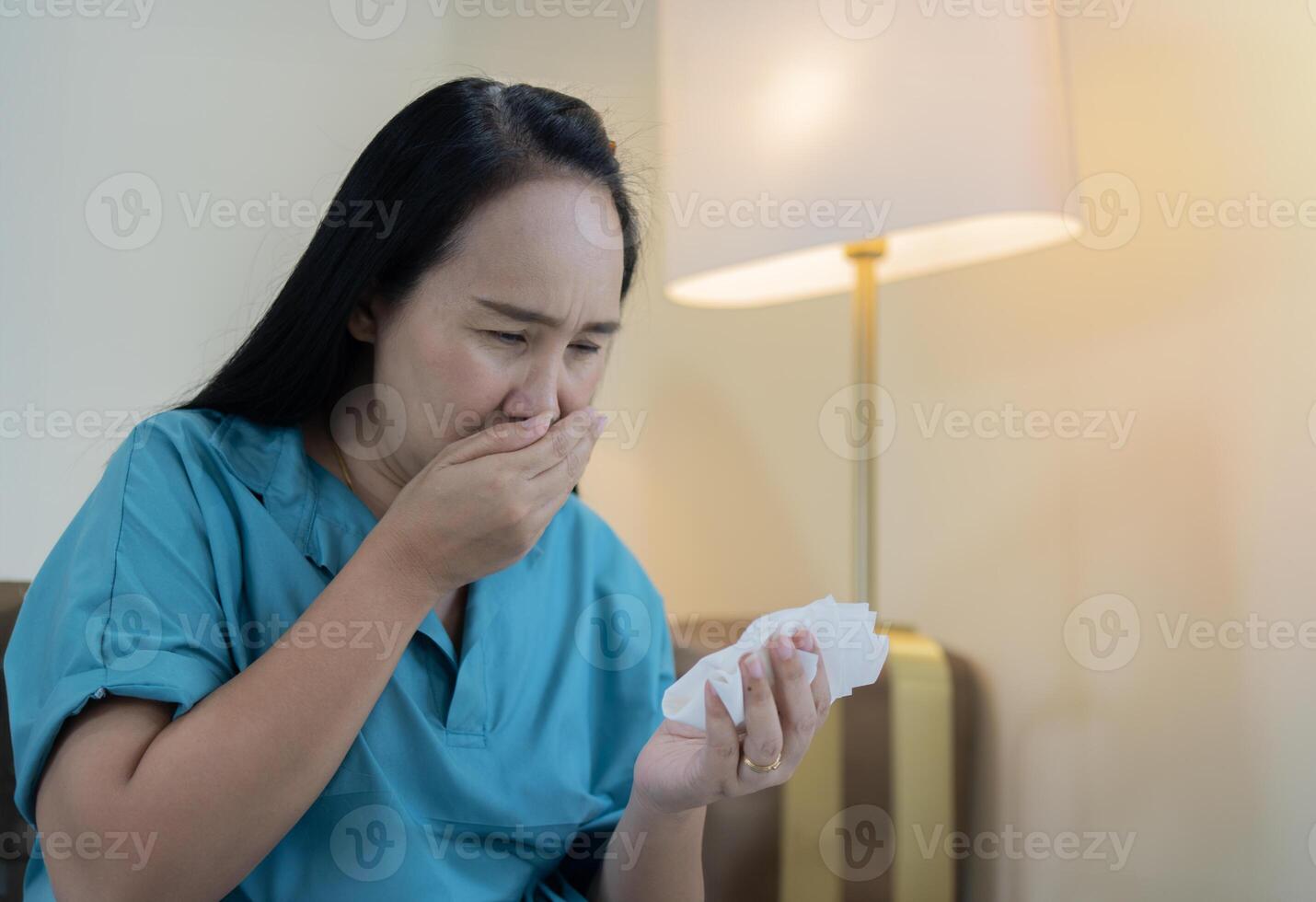 Side view portrait of Asian woman stressed, worry sitting at home and suffering from pneumonia cough photo