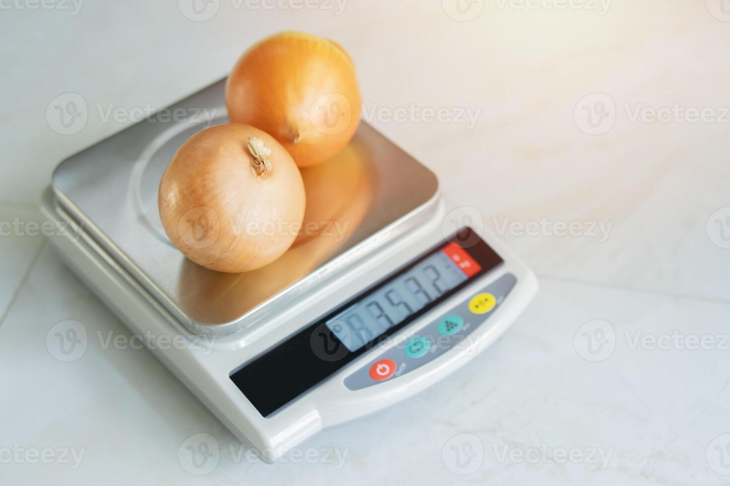 An onions lies on a digital kitchen scale on a marble table with real light from window in kitchen room. photo