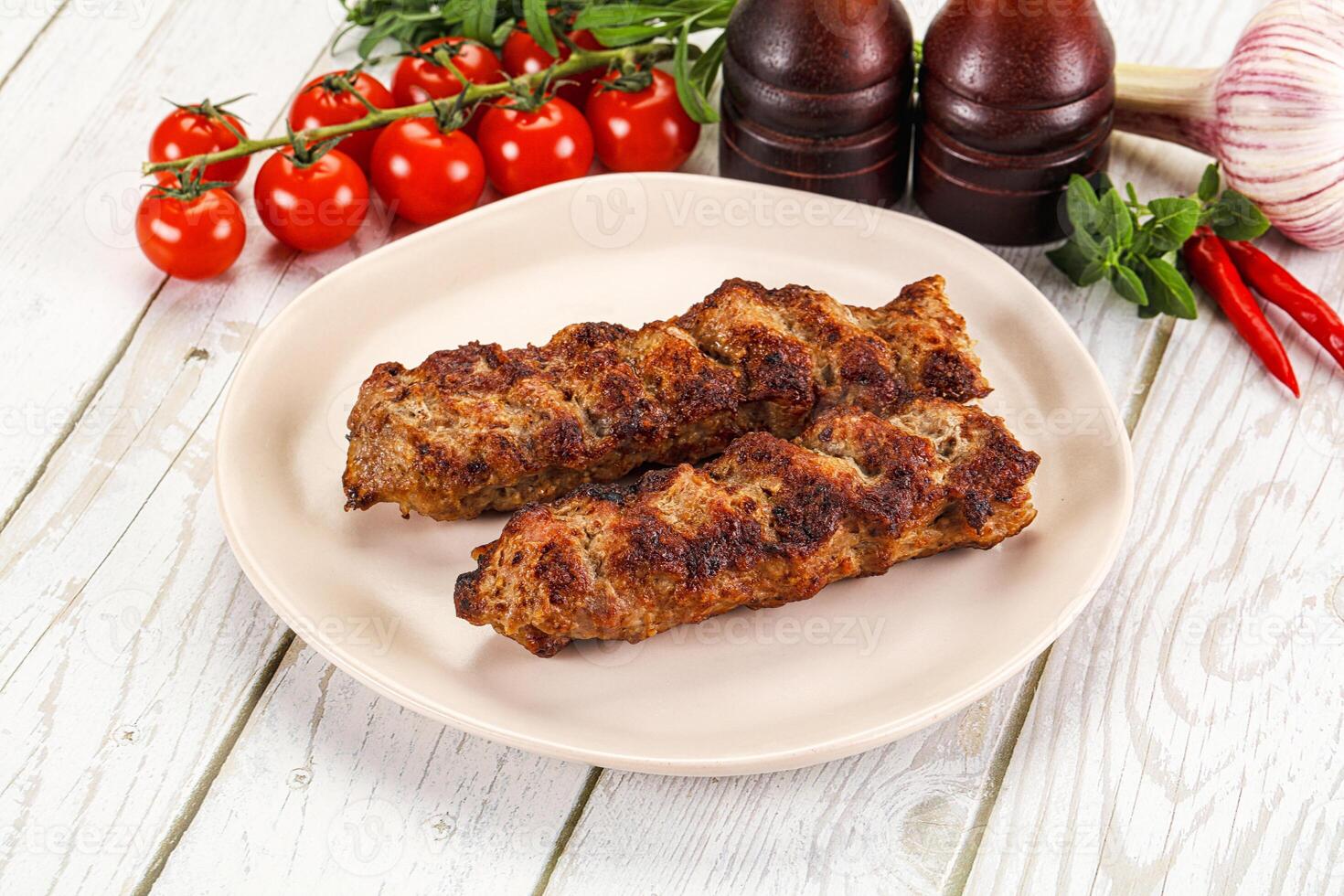 Two meat skewers on a plate with tomatoes and peppers photo