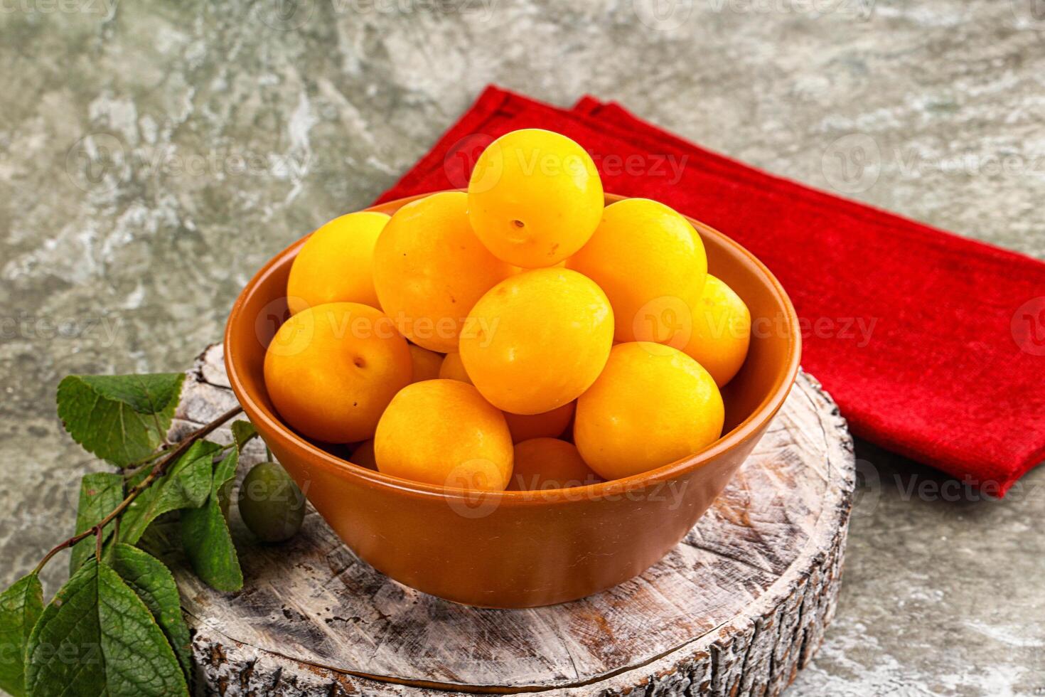 A bowl of yellow plums sitting on a table photo