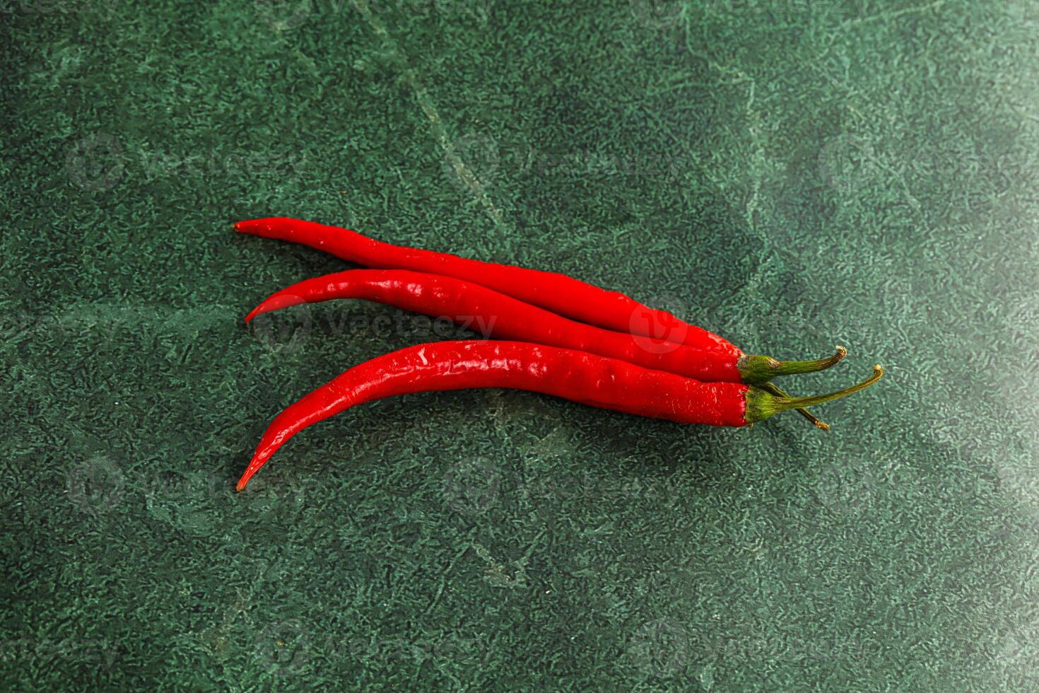 Two red chili peppers on a green surface photo