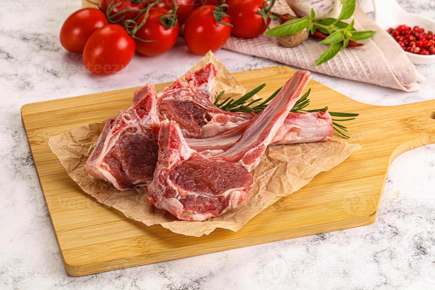 Two lamb chops on a cutting board with tomatoes and herbs photo
