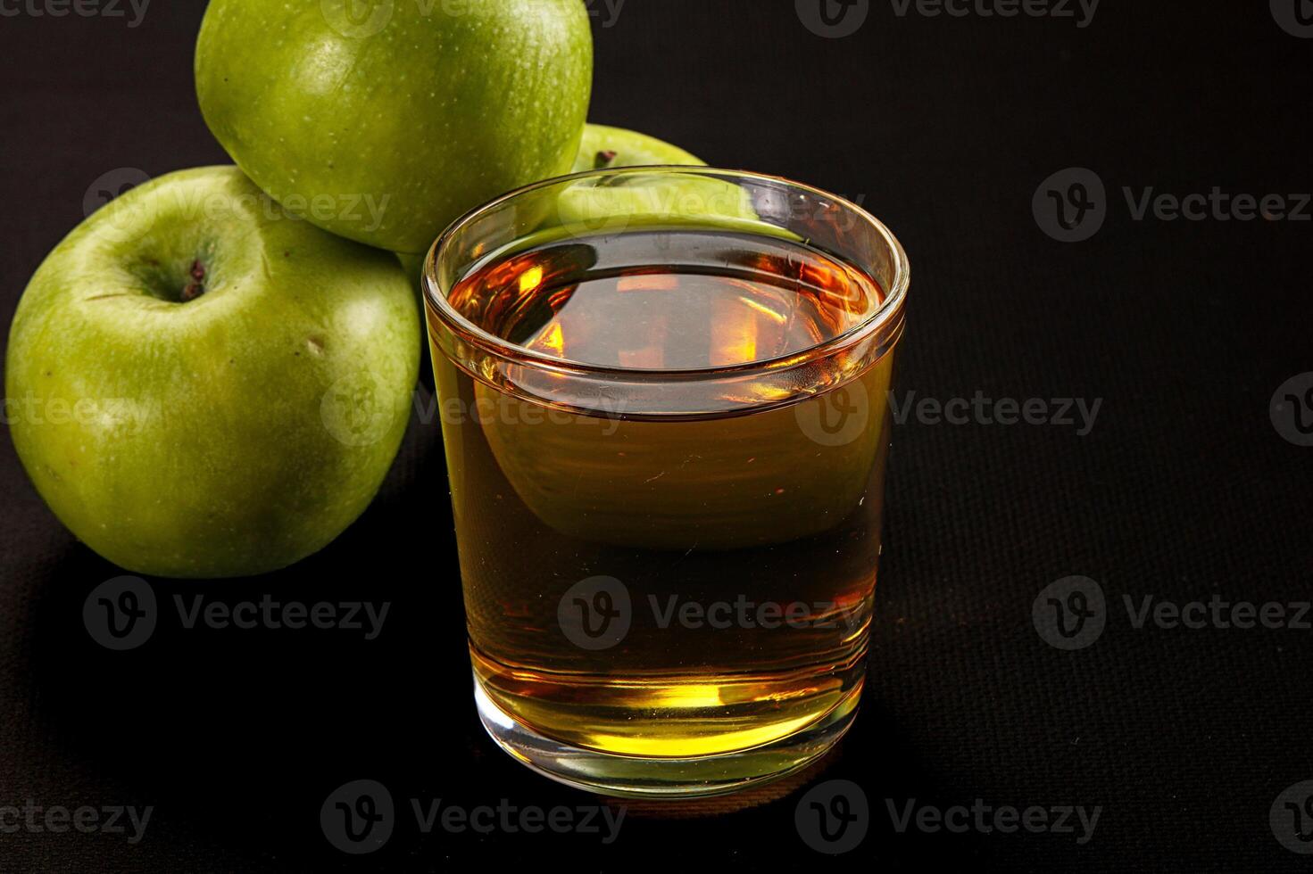 A glass of liquid next to a bunch of green apples photo