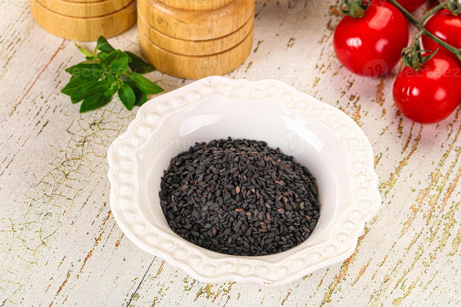 Black sesame seeds in a white bowl on a wooden table photo
