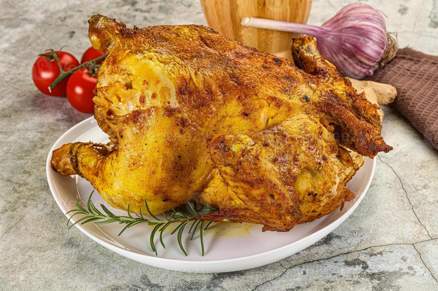 A large roasted chicken on a plate with tomatoes and garlic photo