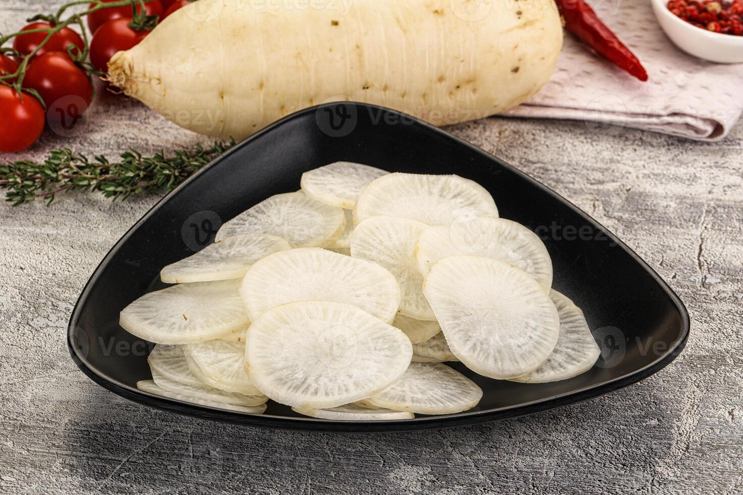 A bowl of sliced radishes on a table next to a bowl of tomatoes photo