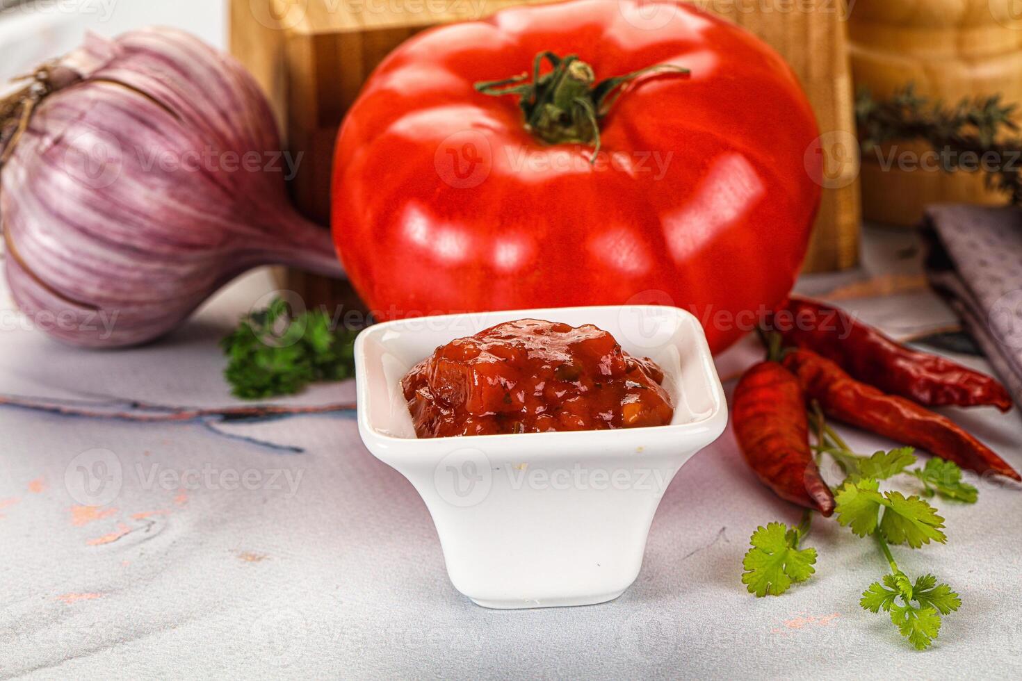 A tomato, onion, and a bowl of chili sauce photo