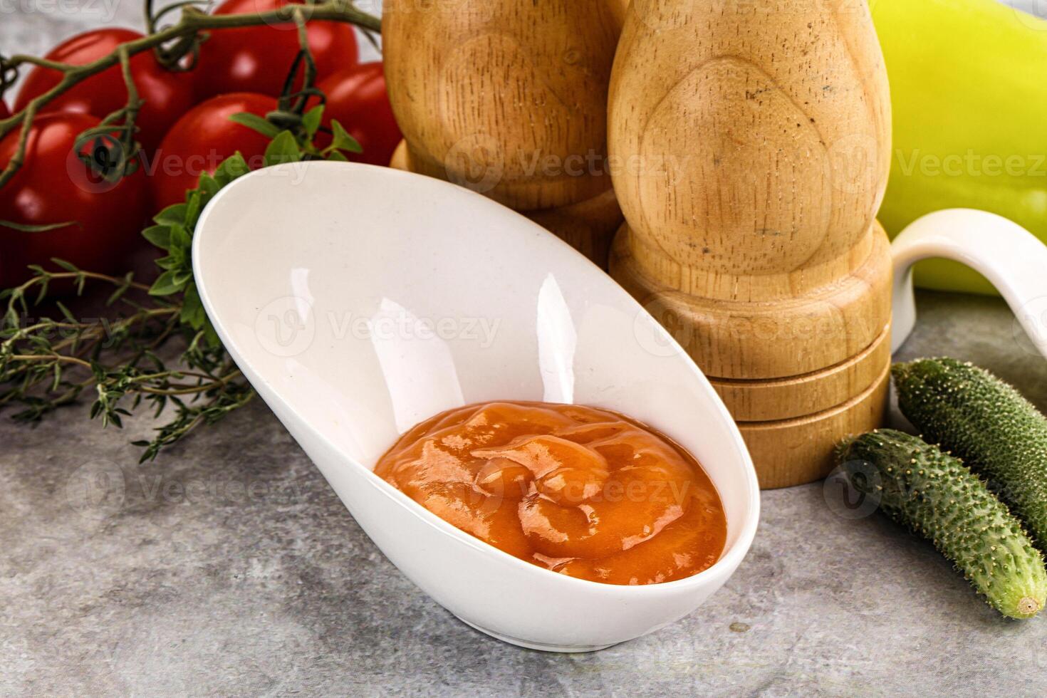 A bowl of tomato sauce next to a pepper and a cucumber photo