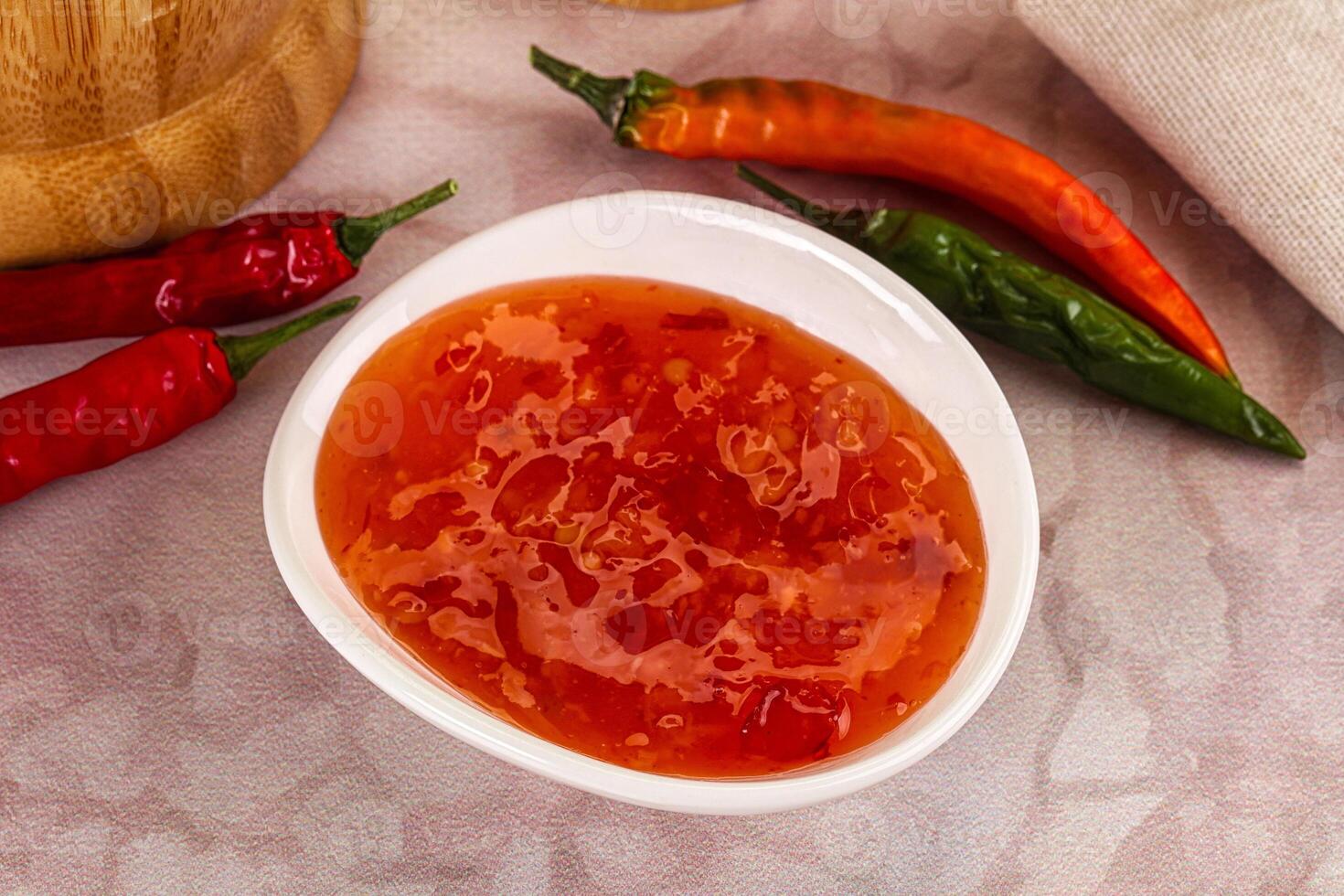 A bowl of chili sauce next to a bowl of chili peppers photo