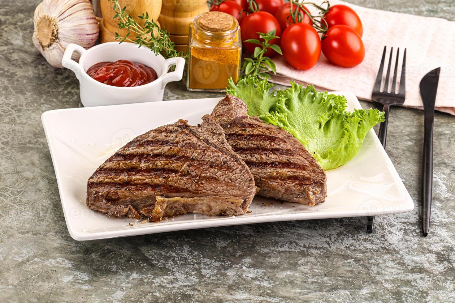 A plate of steak with tomatoes, lettuce and ketchup photo