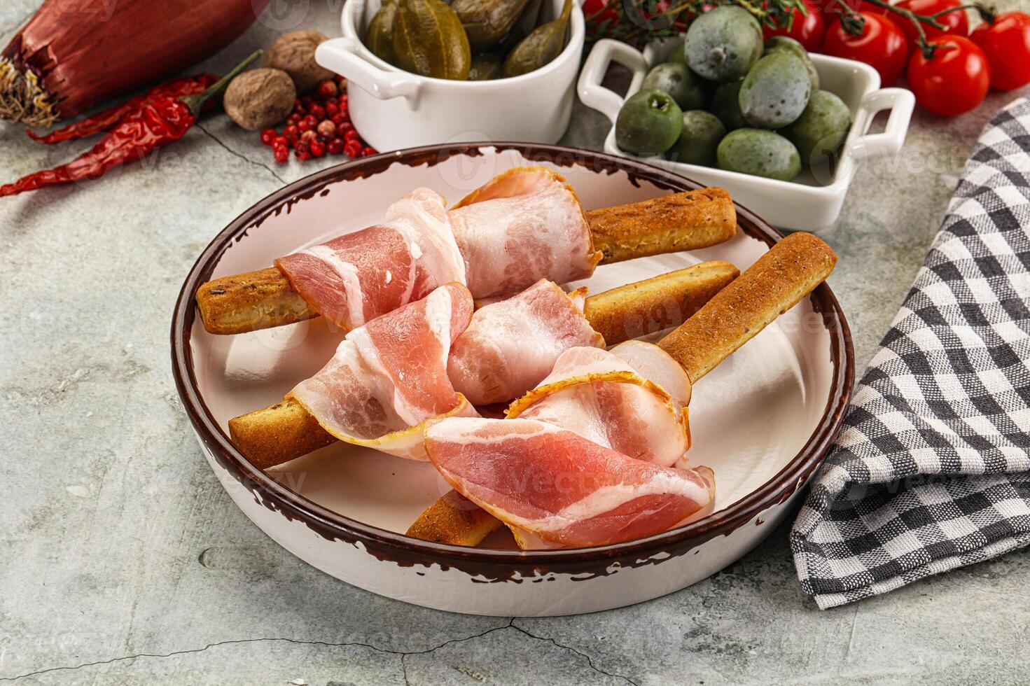 A bowl of food with ham, bread sticks, olives and tomatoes photo