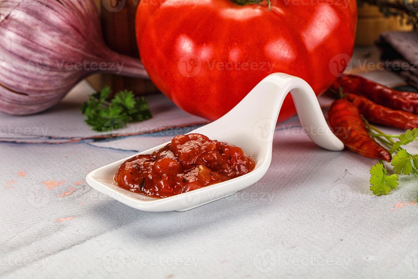 A white measuring spoon with a tomato and some other ingredients photo