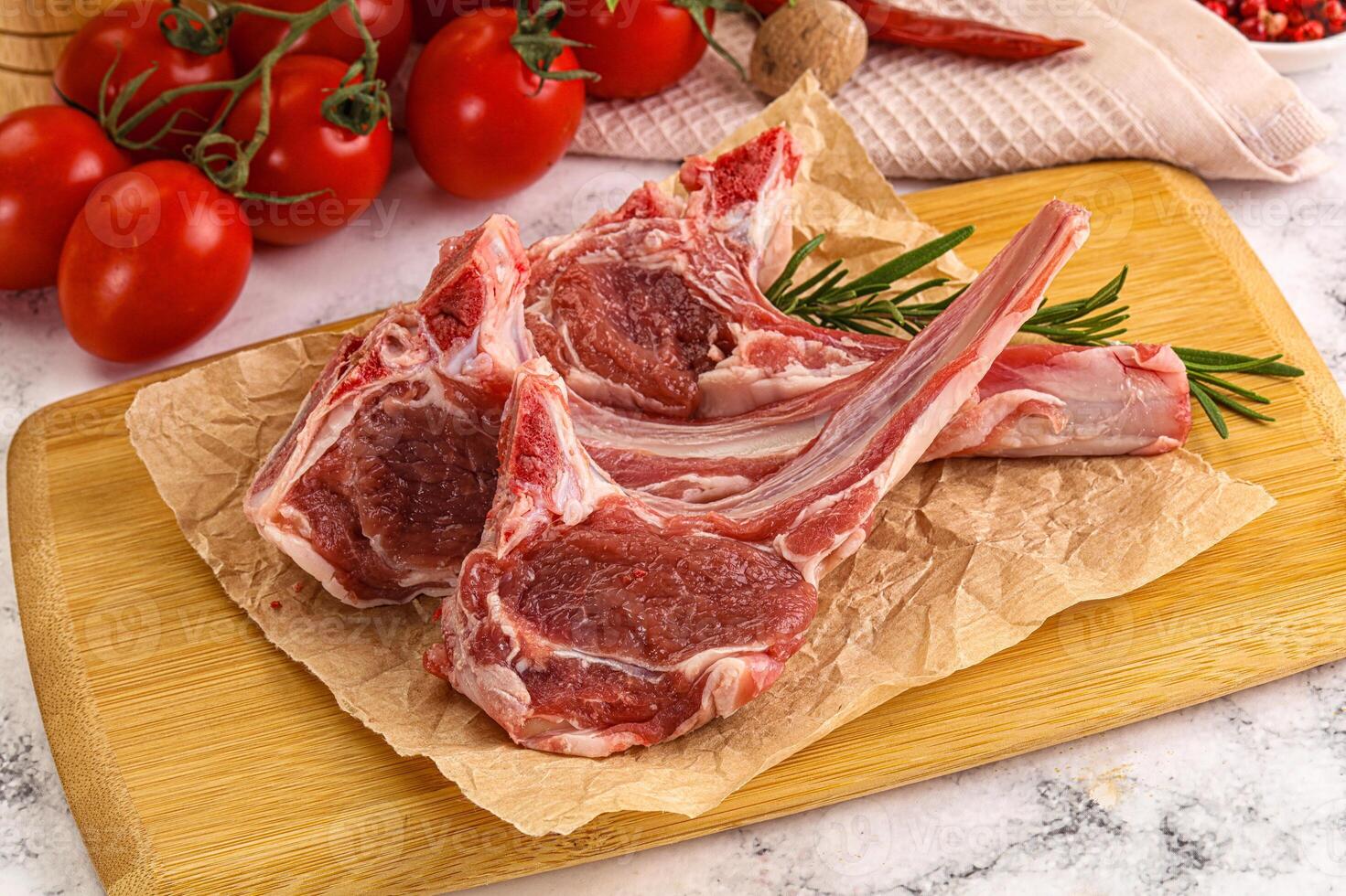 Raw lamb chops on a cutting board with tomatoes photo