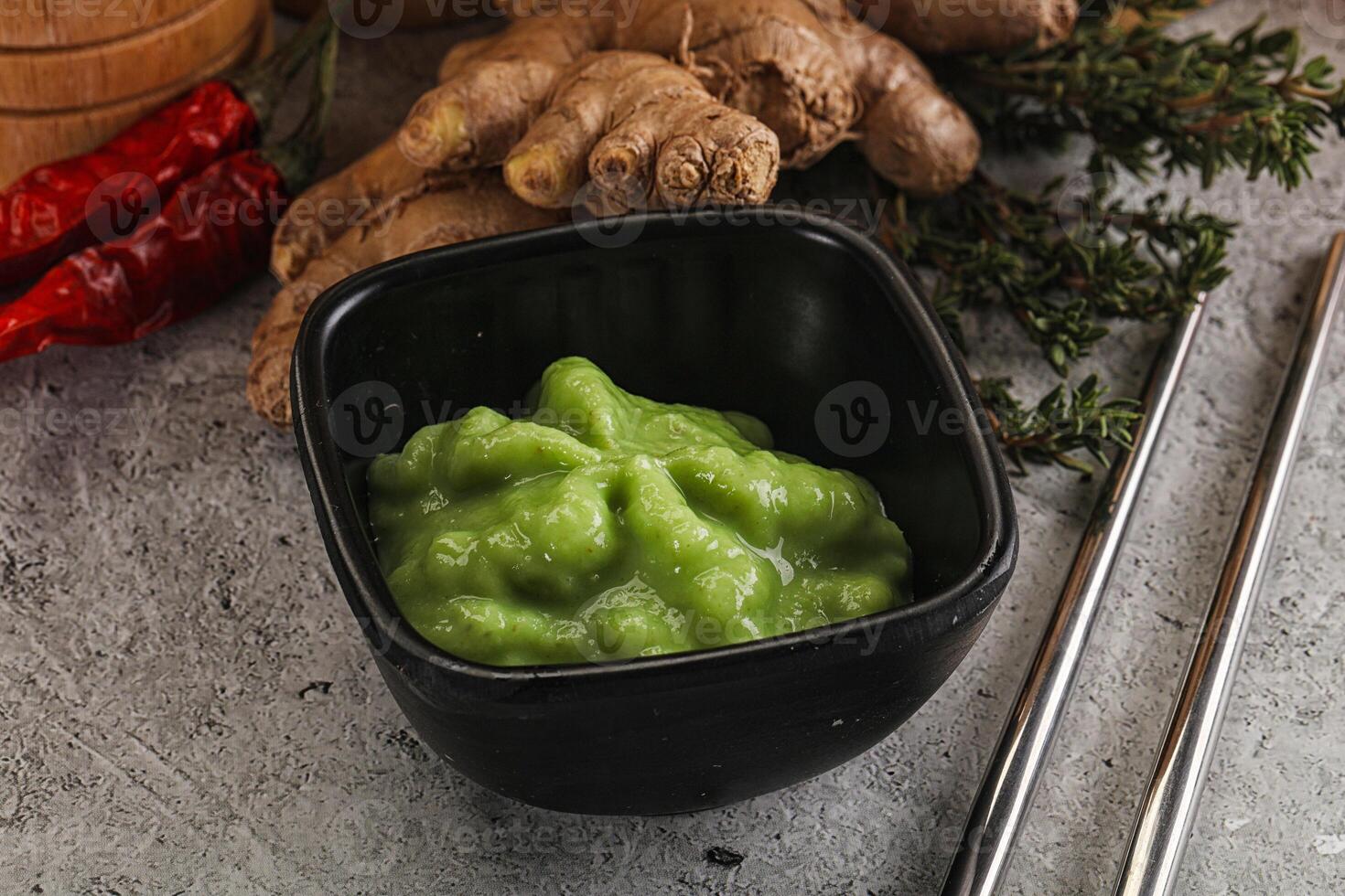 A bowl of green sauce next to some ginger and other ingredients photo