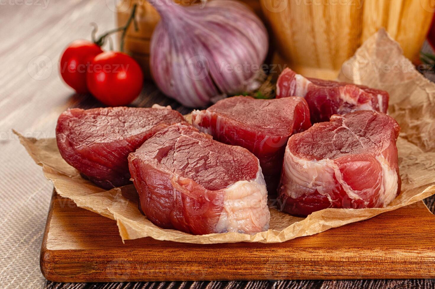 Raw meat on a cutting board with tomatoes and garlic photo