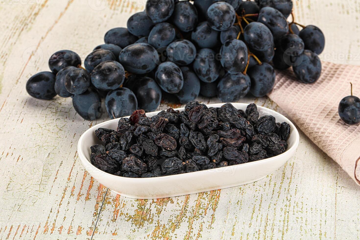 A bowl of black raisins and a bunch of grapes photo