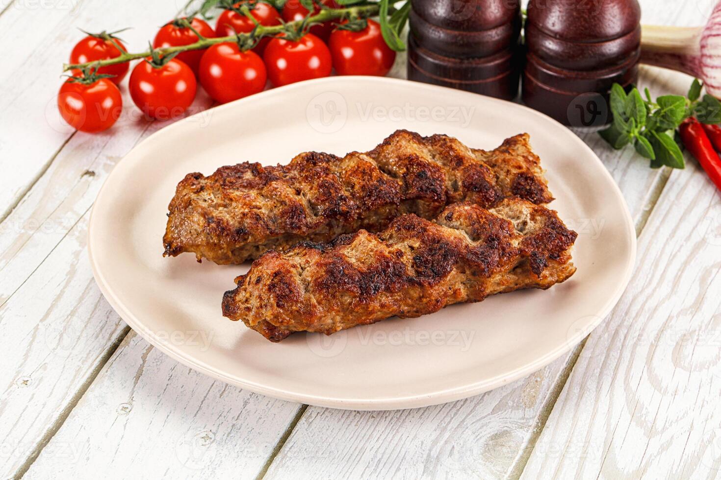 Two meat skewers on a plate with tomatoes and spices photo