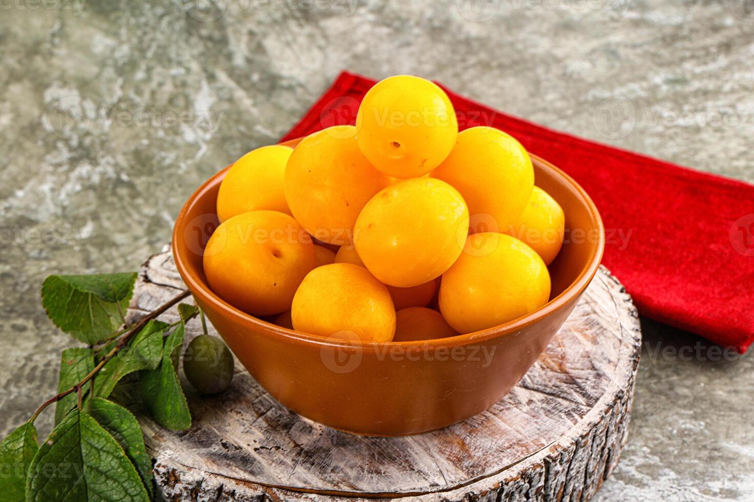 A bowl of yellow plums sitting on a wooden table photo