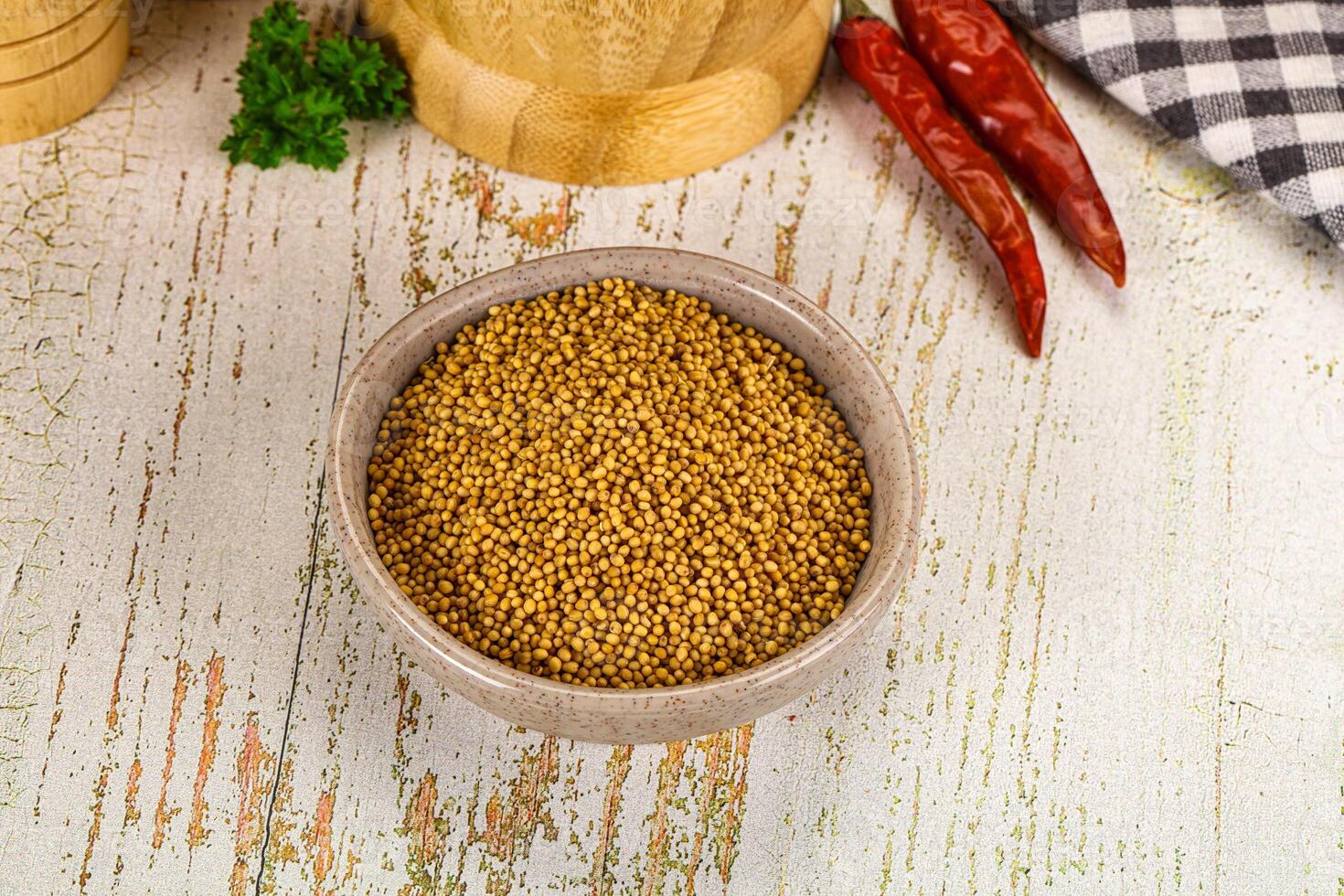 A bowl of mustard seeds and spices on a wooden table photo