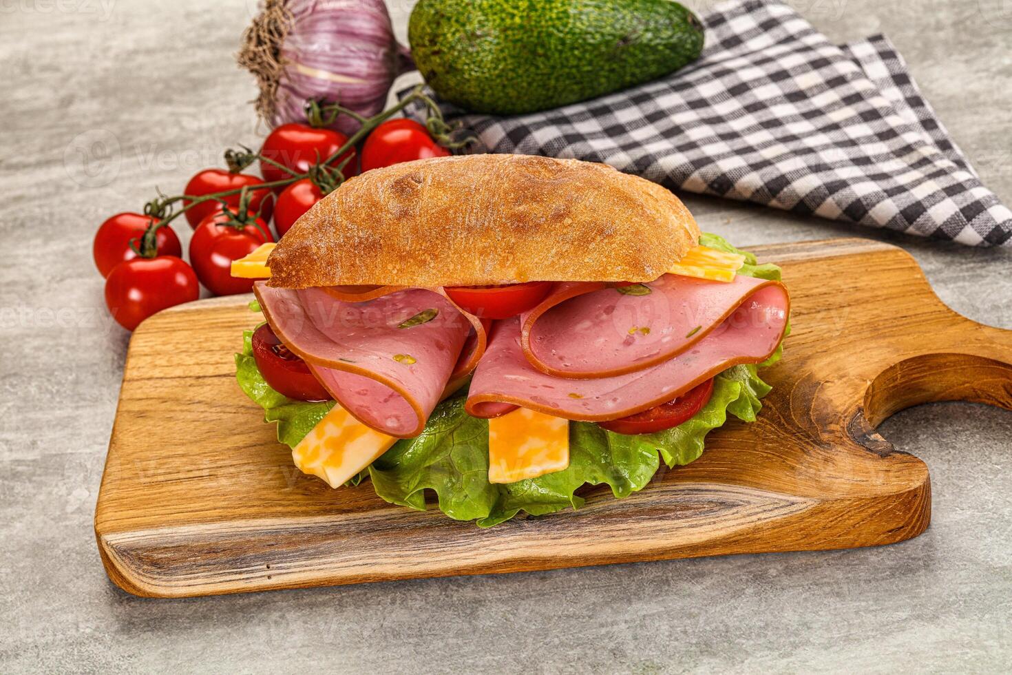A sandwich with ham, cheese and tomatoes on a wooden cutting board photo