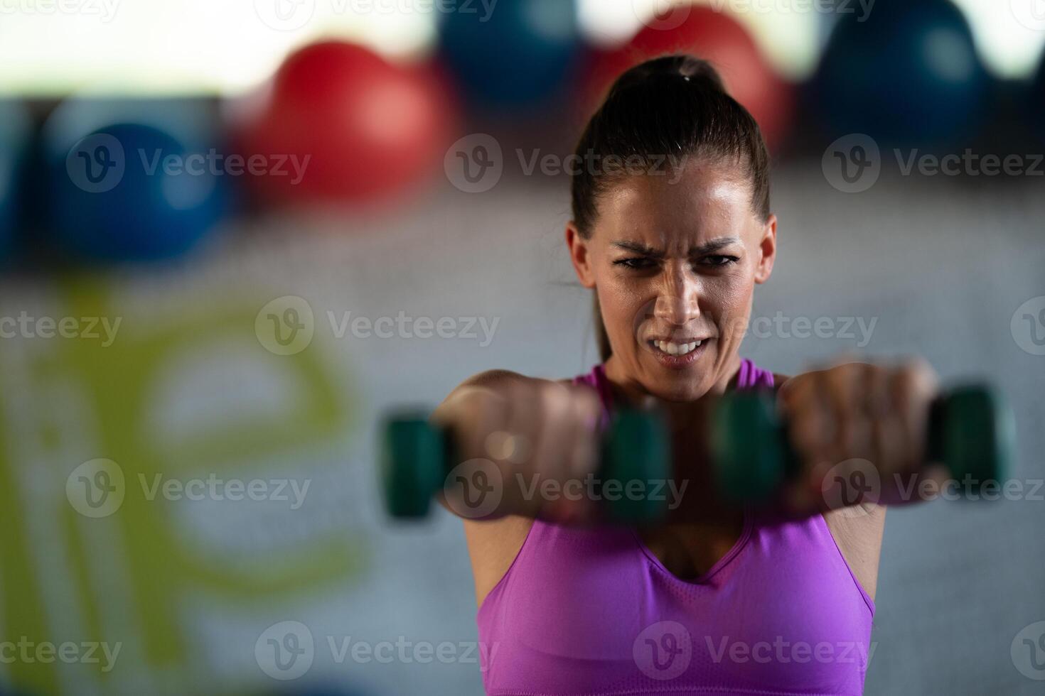 A focused and determined woman performs a strength building dumbbell workout at the gym, showcasing her athletic physique and dedication to fitness. photo