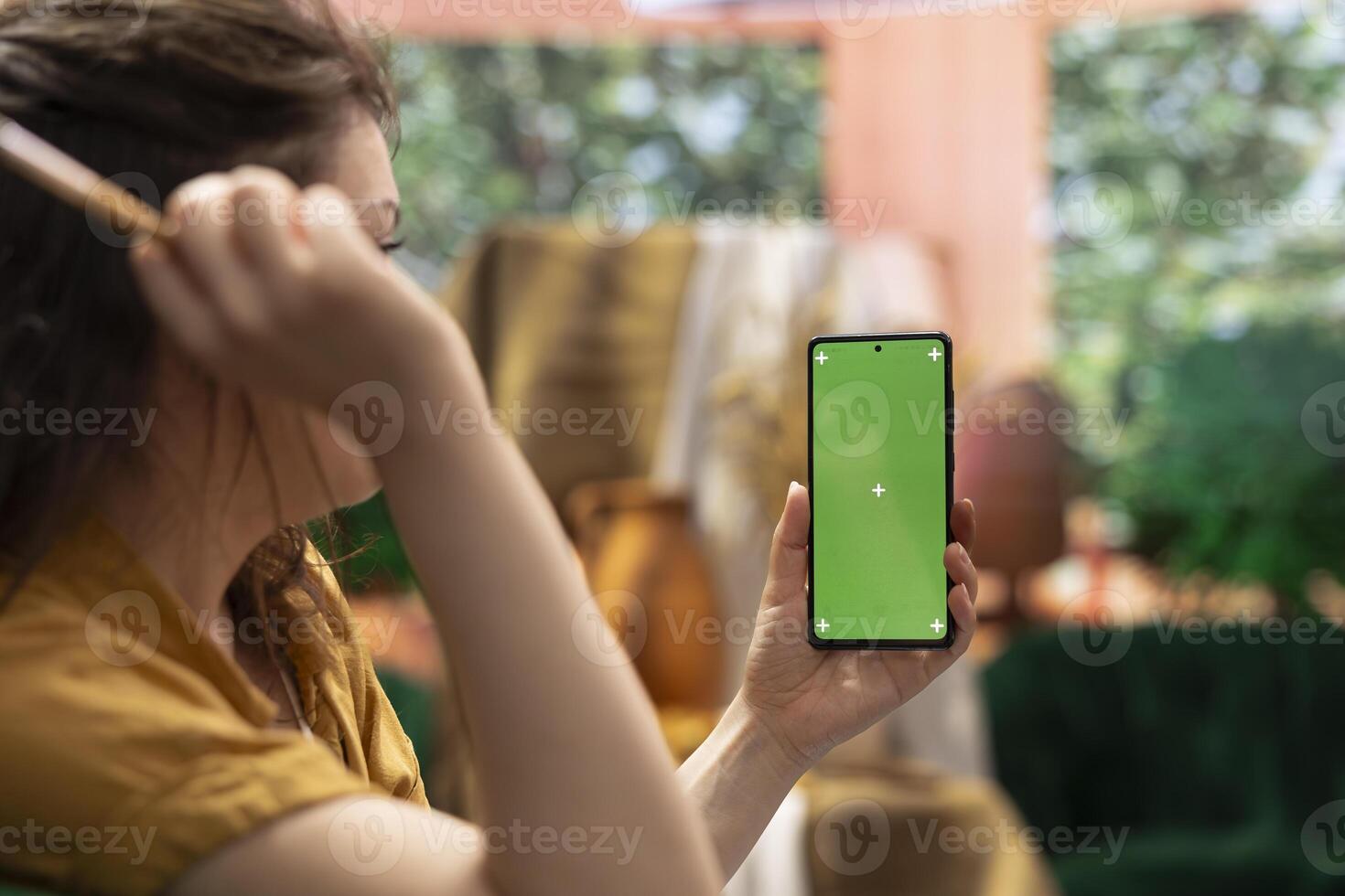 Painter holding a device with isolated mockup screen in her art studio, looking at her finished masterpiece with oil paints on canvas. Beautiful rustic artwork for a fine art gallery, creativity. photo
