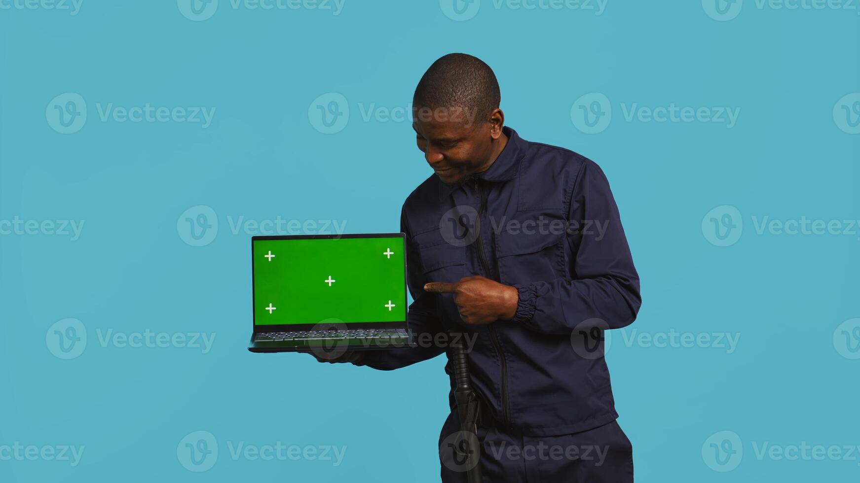 Portrait of happy security guard at work showcasing green screen laptop while overseeing premises. Cheerful private law enforcement worker presenting chroma key notebook, studio backdrop, camera B photo