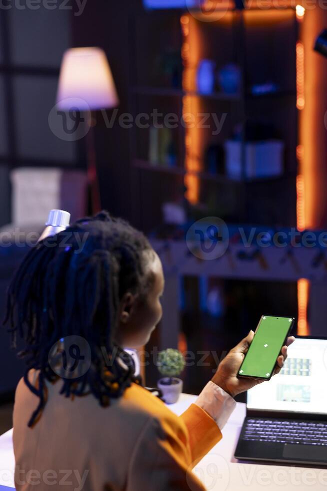 Green screen smartphone used by woman at laptop desk answering phone call while checking emails displayed on screen. Mockup cellphone used by girl in telephone call with friend photo