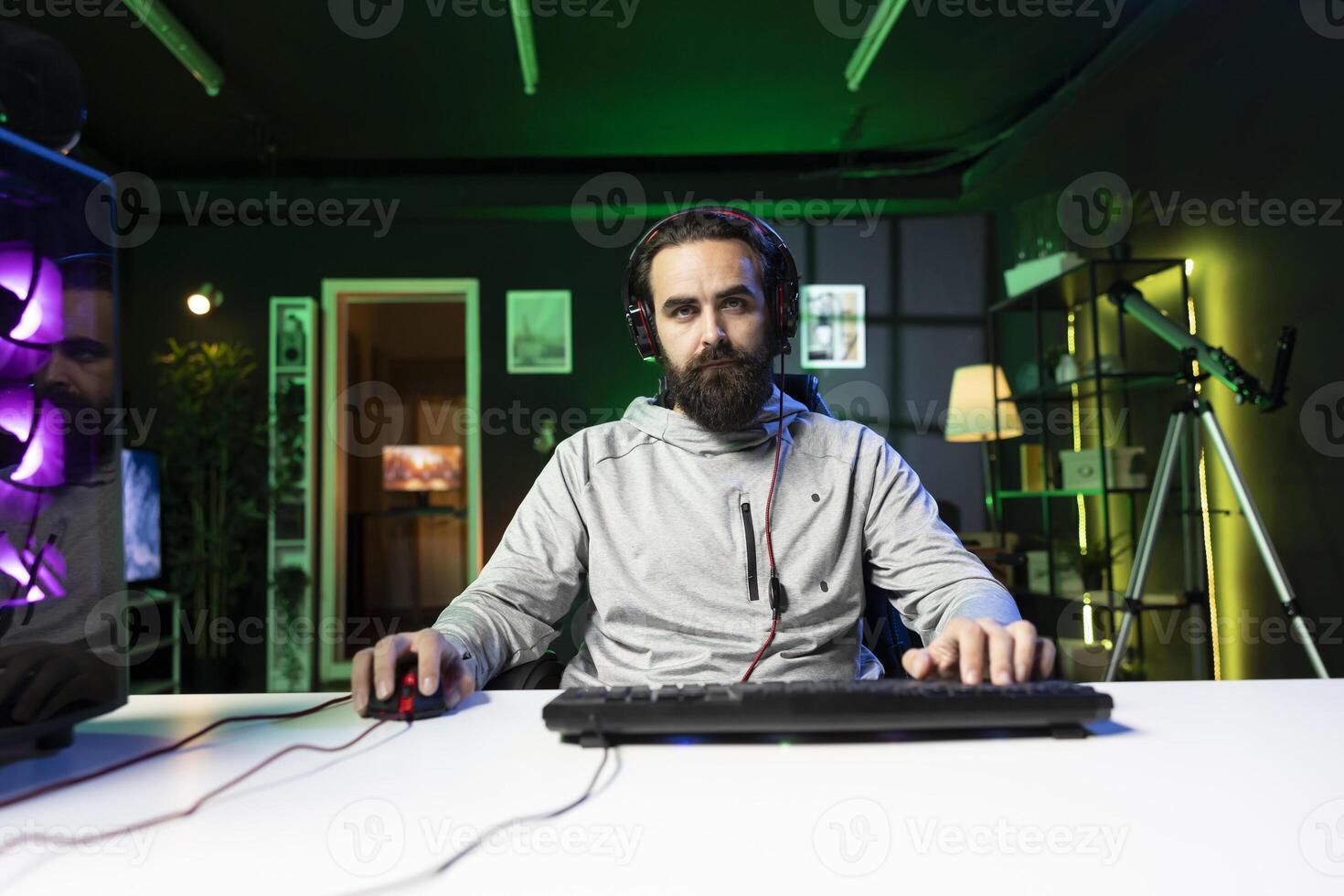 Esports player wearing headphones recording himself playing videogames in front of online viewers during livestream, providing commentary. Pro gamer streaming gaming session, talking in mic photo