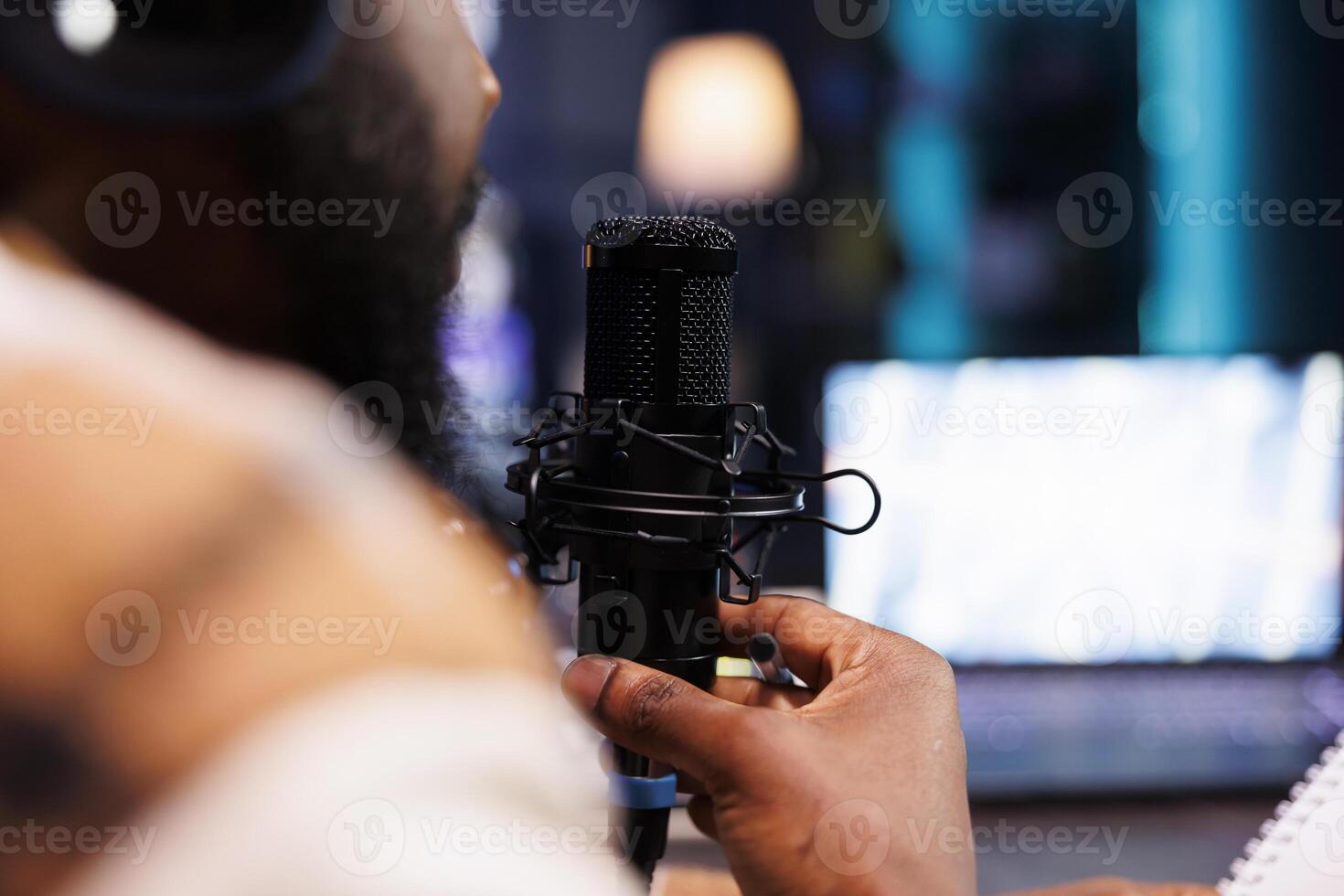 Closeup of african american person with a beard speaking into a microphone creating asmr content. Detailed view of black man using modern audio equipment to create a podcast episode at home. photo