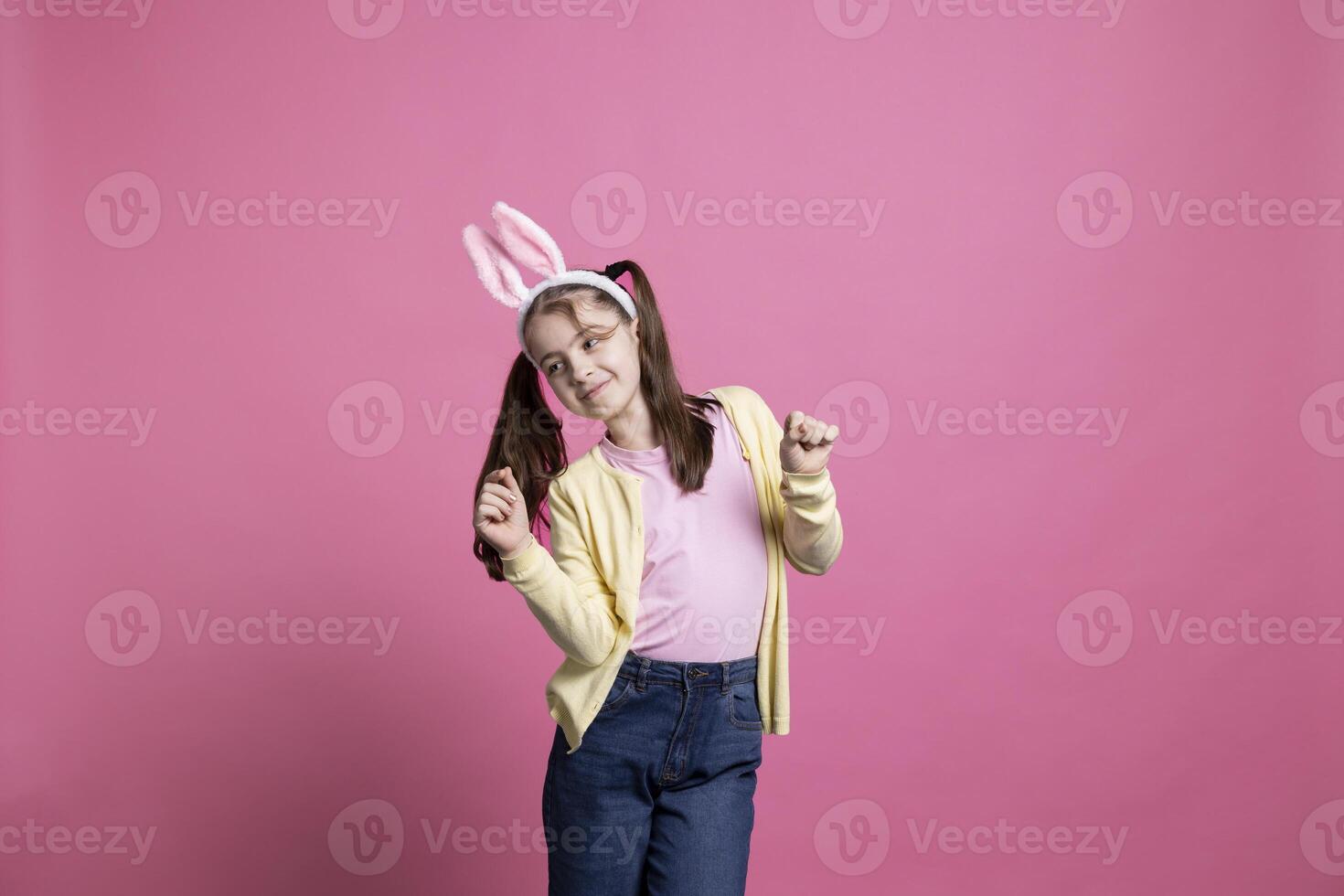 Joyful and energetic child moving around and performing dance moves while wearing bunny ears in a studio. Young girl expressing enthusiasm and happiness for the Easter celebration. photo
