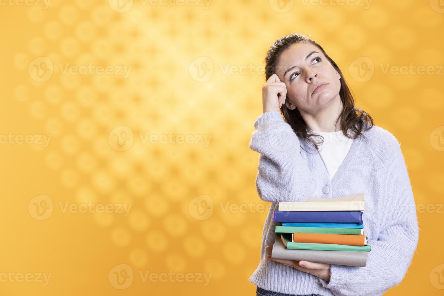 Portrait of woman daydreaming while holding books, thinking of characters. Person with stack of novels in arms caught in imagination while enjoying leisure time, isolated over studio background photo