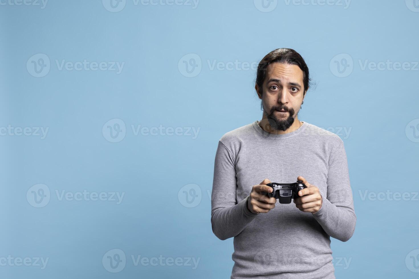 Middle eastern man playing games online on his console, attending an electronic cyber tournament against blue background. Young adult having fun with a shooter in studio, controller. photo