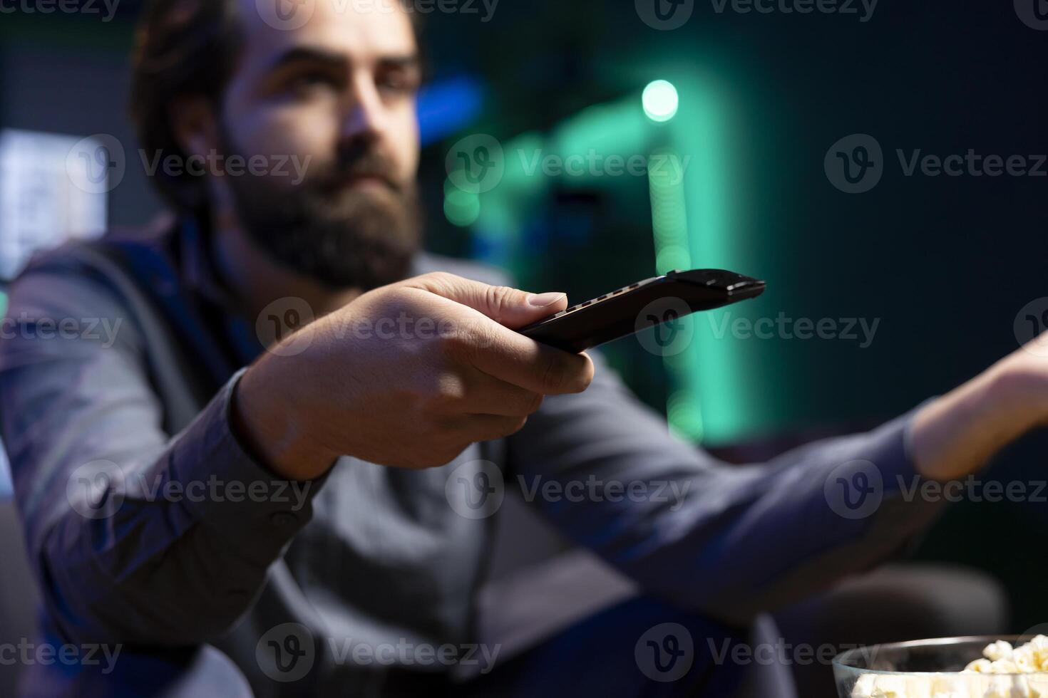Tired man zapping through channels, watching news broadcast while resting in living room, enjoying leisure. Person using remote control to select TV station, close up shot photo